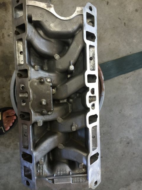 1989 Ford Bronco - An aluminum engine intake manifold is shown from a top-down perspective, with a person's foot visible in the lower left corner.