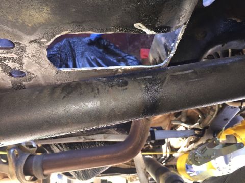 1989 Ford Bronco - Hole cut into the frame rail of a vehicle's underbody, with exhaust pipe visible.