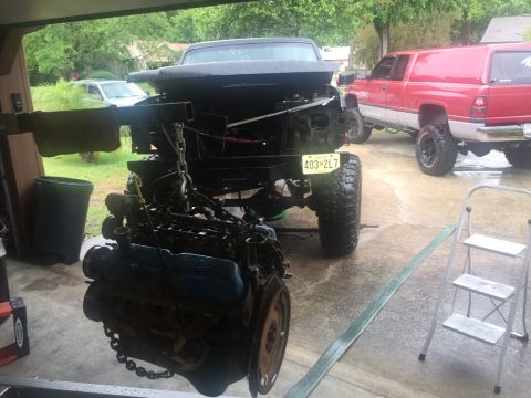 1989 Ford Bronco - An engine is suspended by a chain, ready for removal or installation, with a truck and a red pickup visible.
