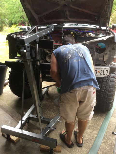 1989 Ford Bronco - Engine hoist is positioned over a vehicle's engine bay as a man works on it.
