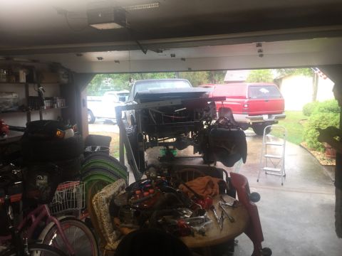 1989 Ford Bronco - A disassembled truck sits in a garage, with other vehicles parked outside.