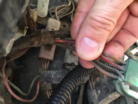 1989 Ford Bronco - Close-up of a hand manipulating wires within a vehicle's complex electrical harness.