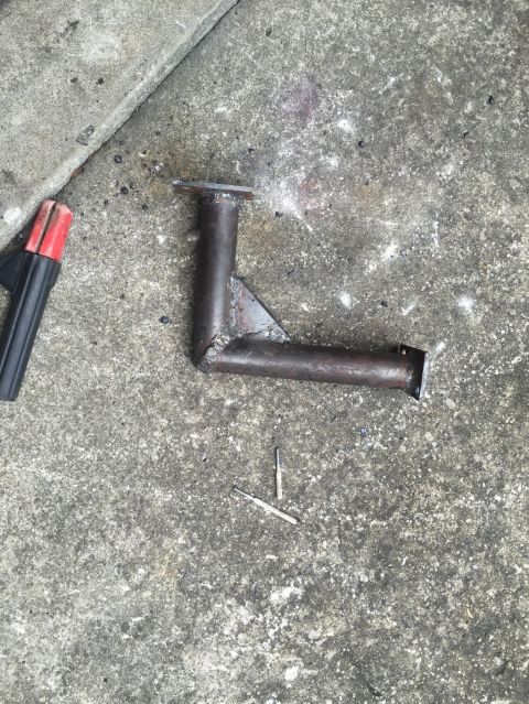1989 Ford Bronco - A custom-fabricated metal bracket, likely for automotive modification, is shown on a concrete surface next to welding leads.