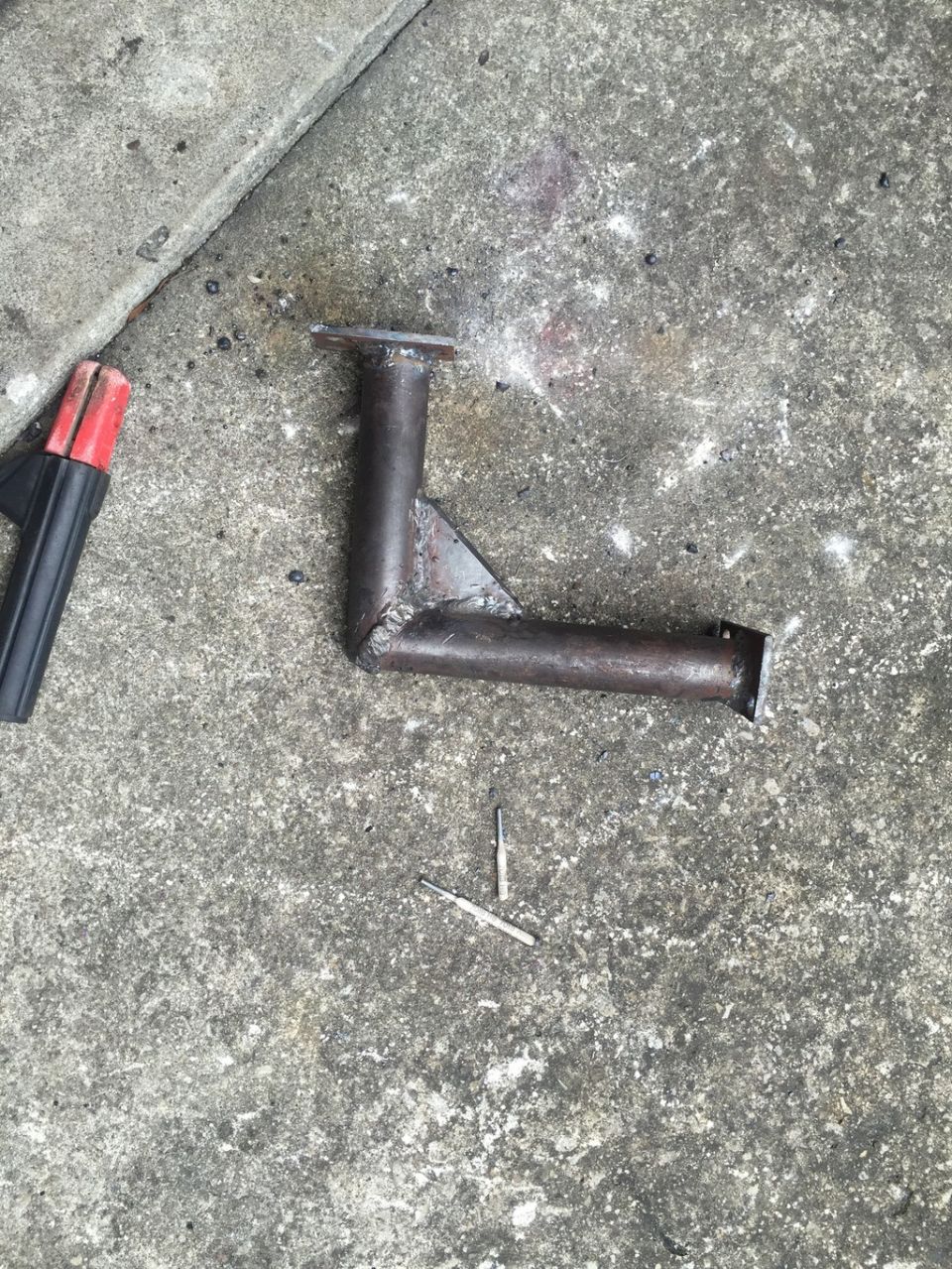 Custom metal bracket with welded joints and mounting flanges, resting on concrete