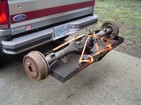 1989 Ford Bronco - A rear axle assembly is secured with orange straps to a trailer attached to a Ford truck.