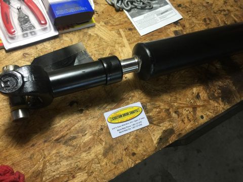 1989 Ford Bronco - A custom driveshaft is shown on a wooden surface, with tools and a chain in the background.