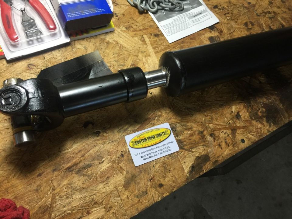 Custom driveshaft on a workbench with tools and a chain nearby. Sticker says 'Custom Drive Shafts'