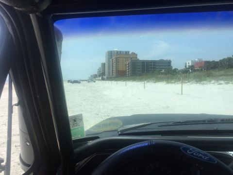 1989 Ford Bronco - View from inside a vehicle on a beach, looking towards buildings and the ocean.