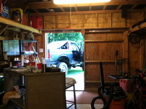 1989 Ford Bronco - A blue SUV is parked inside a cluttered garage with its doors open.