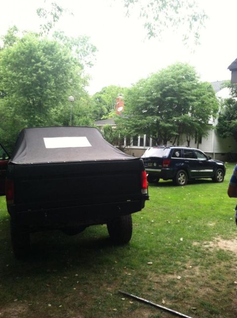 1989 Ford Bronco - Rear view of a black pickup truck with a soft top, with a dark SUV in the yard.