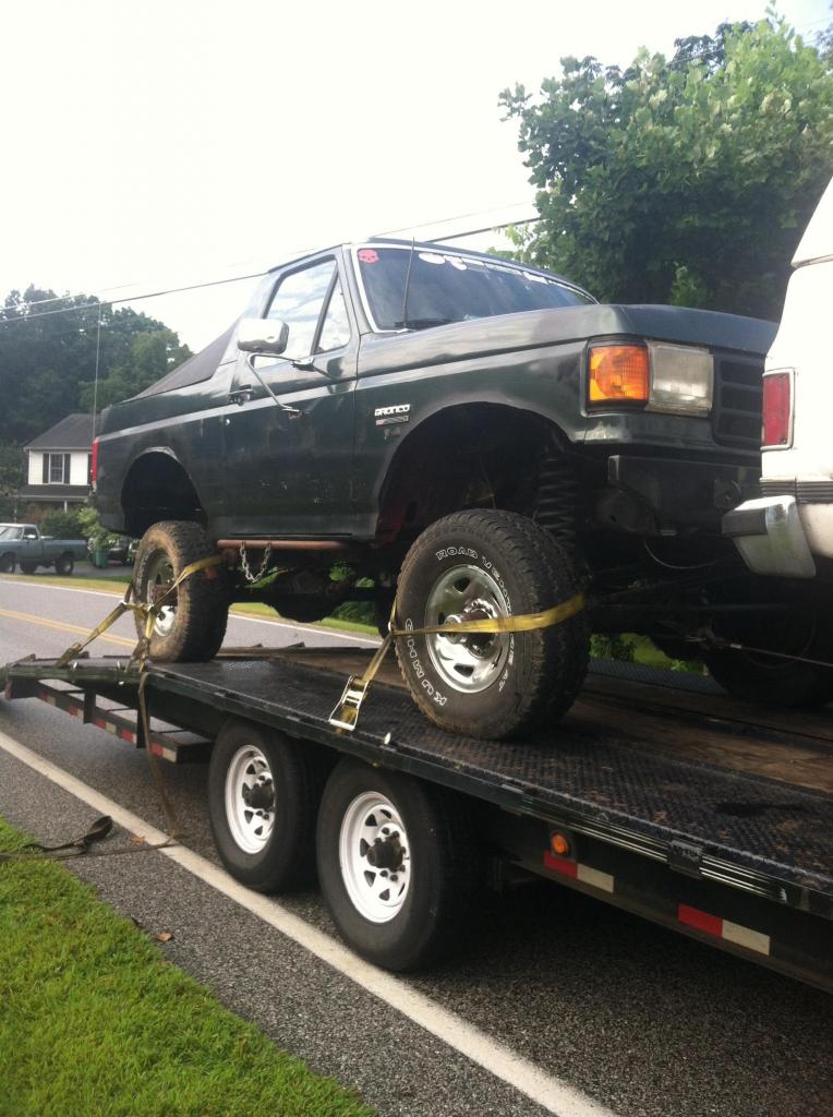 Dark green Ford Bronco on a flatbed trailer, lifted with large tires