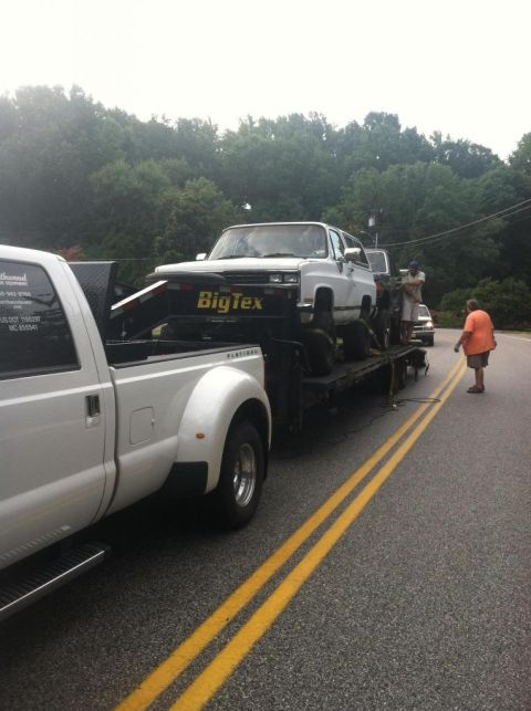 1989 Ford Bronco - A white SUV is loaded onto a flatbed tow truck on a road.