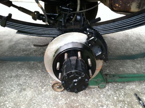 1989 Ford Bronco - Close-up of a vehicle's rear brake assembly, a black caliper and hub, with leaf springs visible overhead.
