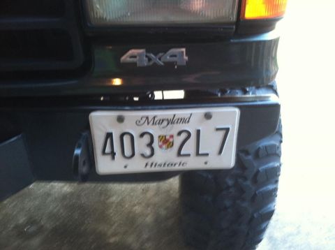 1989 Ford Bronco - A close-up view of the front bumper and license plate of a dark-colored vehicle, featuring a Maryland license plate that reads "403 2L7 His…