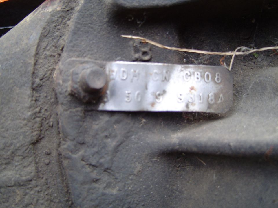 Stamped metal axle identification tag bolted to a dirty cast axle housing