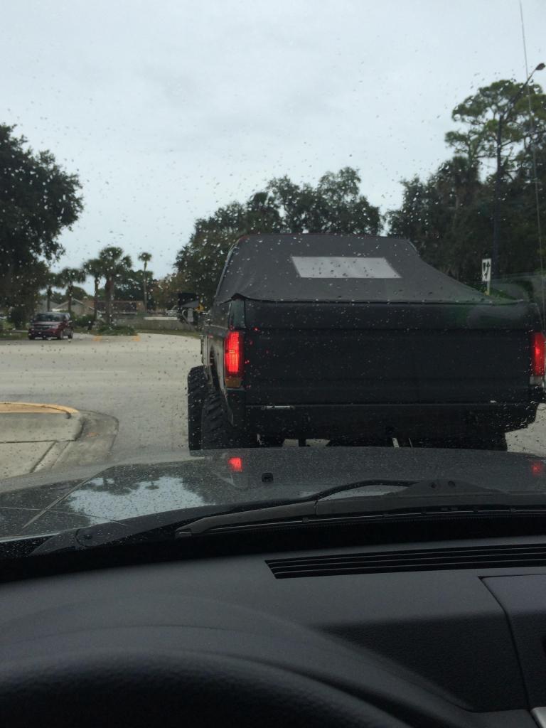 Rear view of a black Ford Bronco with a soft top and large tires on a rainy day.