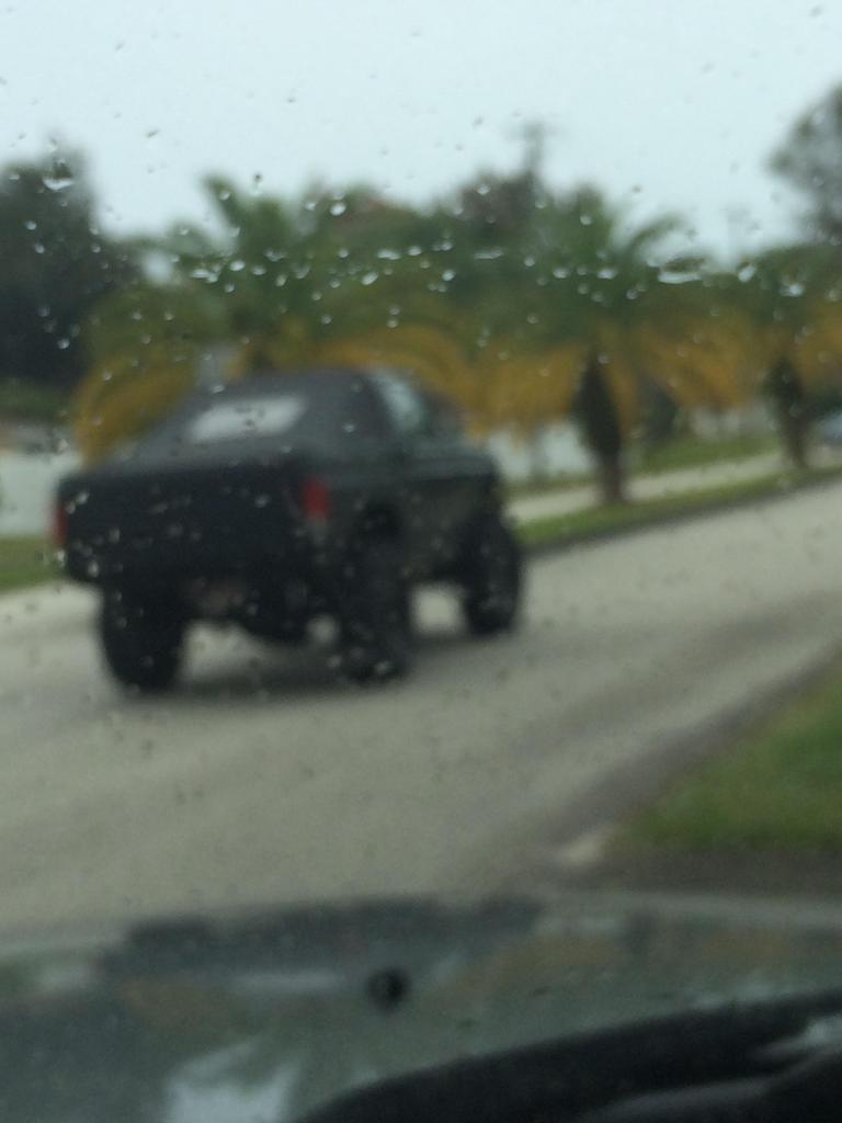 Black Ford Bronco driving on a street in the rain.