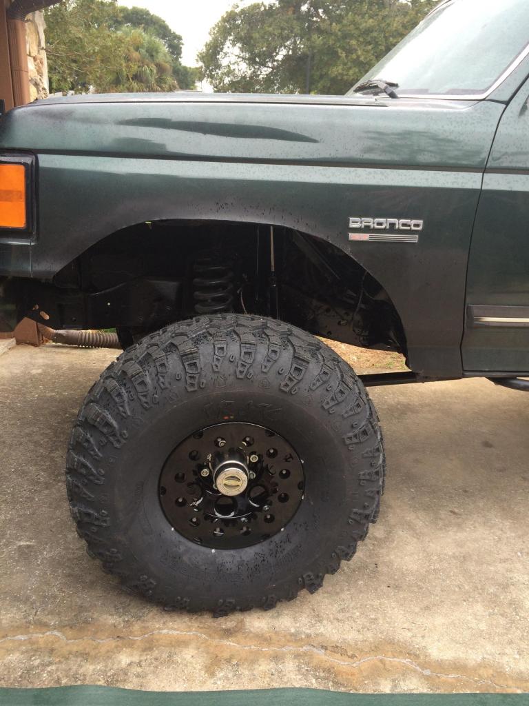 Dark green Ford Bronco with lifted suspension and large off-road tire, front driver's side view.