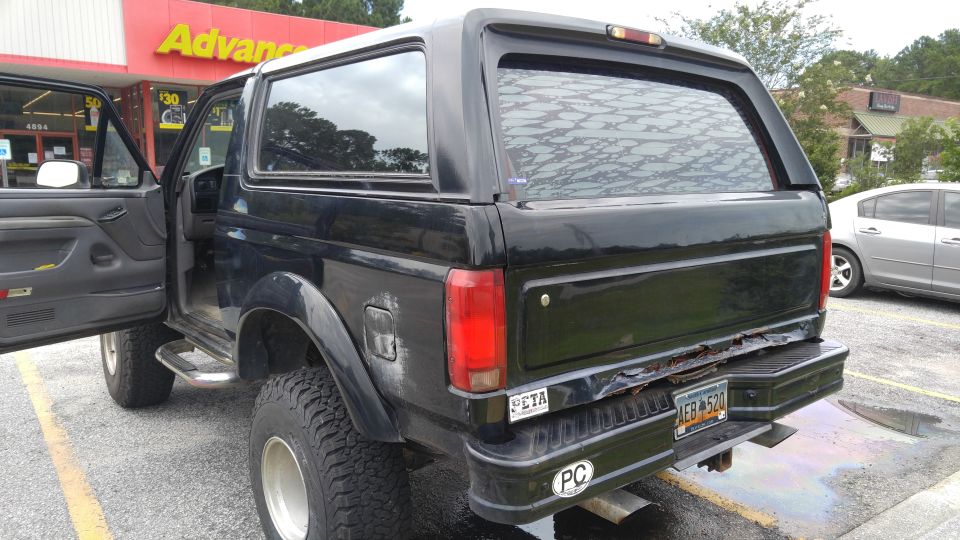 Black Ford Bronco with driver's door open, showing off-road tires and rusted bumper.