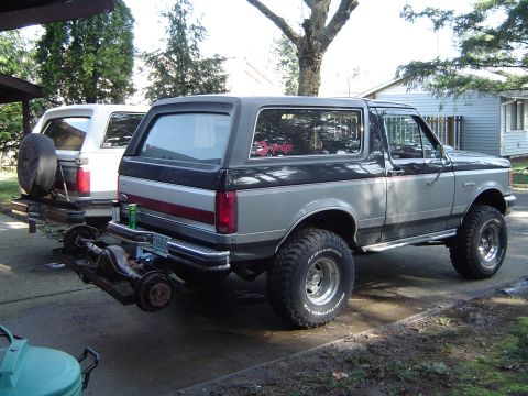 1989 Ford Bronco - Two-tone 1989 Ford Bronco parked outside with another Bronco and a trailer hitch carrying an axle.