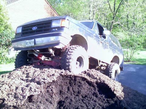 1989 Ford Bronco - This lifted Ford Bronco is positioned on a pile of dirt, showing its off-road capabilities.