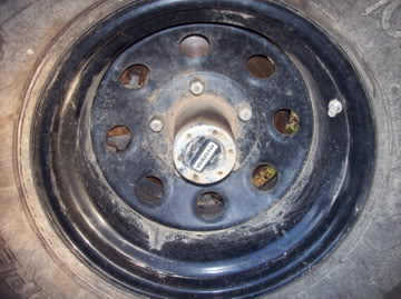 1989 Ford Bronco - A close-up view of a black steel wheel with a Warn manual locking hub on a 1989 Ford Bronco. The wheel is dirty and shows signs of wear.