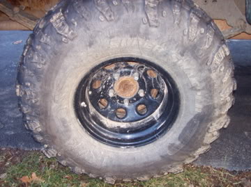 1989 Ford Bronco - A close-up, low-angle shot shows the front driver's side tire and black steel wheel of a vehicle. The tire is heavily treaded and appears t…