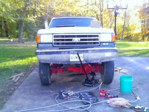 1989 Ford Bronco - The front end of a lifted, white Ford truck or SUV is shown parked on a concrete driveway with a basketball hoop in the background. A red s…