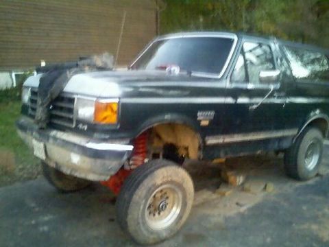 1989 Ford Bronco - A dark colored Ford Bronco is shown with its front end raised on blocks and red suspension components visible. The vehicle appears to be un…
