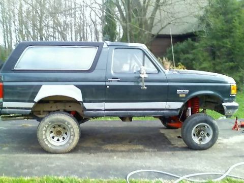 1989 Ford Bronco - The side view of a dark green Ford Bronco is shown with a lifted suspension and large tires. The vehicle appears to be undergoing modificat…