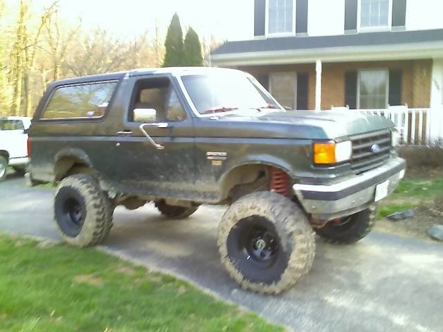 Lifted dark green 1989 Ford Bronco with large tires parked on a driveway.