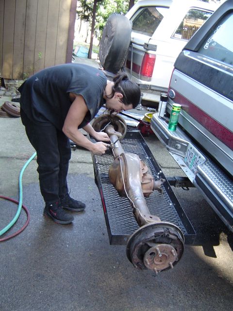 1989 Ford Bronco - A person works on a rear axle assembly on a trailer, with two vehicles in the background.