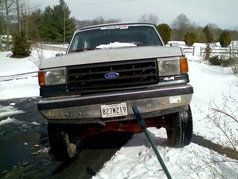 1989 Ford Bronco - The front view of a white and green Ford truck is parked in a snowy driveway. The vehicle has a Maryland license plate that reads "827M219".