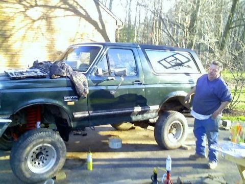 1989 Ford Bronco - A man stands next to a dark green Ford Bronco that appears to be undergoing maintenance, with tools and parts visible around it. The vehicl…
