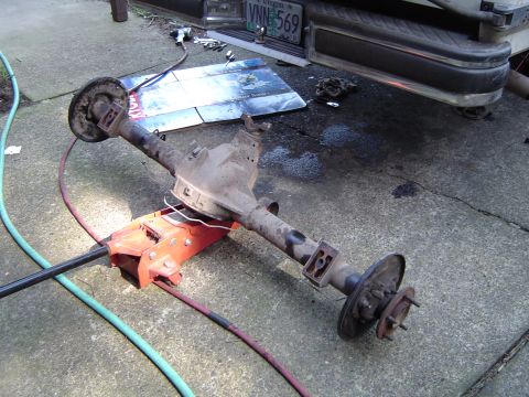 1989 Ford Bronco - A rear axle assembly is shown on an orange jack, with a white truck in the background and tools on the ground.