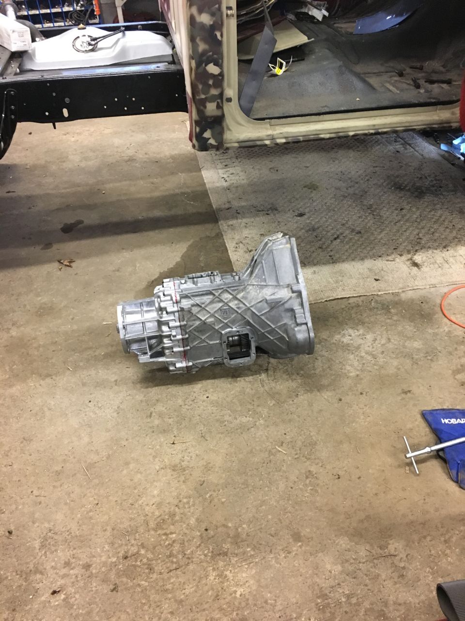 Silver transmission on concrete floor in front of classic pickup truck interior.
