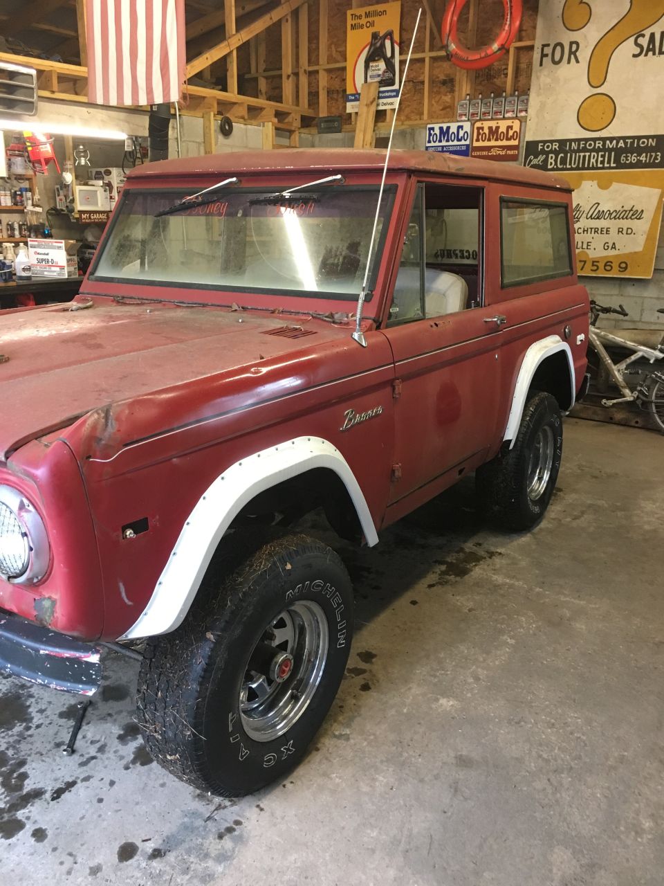 Red 1974 Ford Bronco with white fender flares and chrome wheels in a garage.