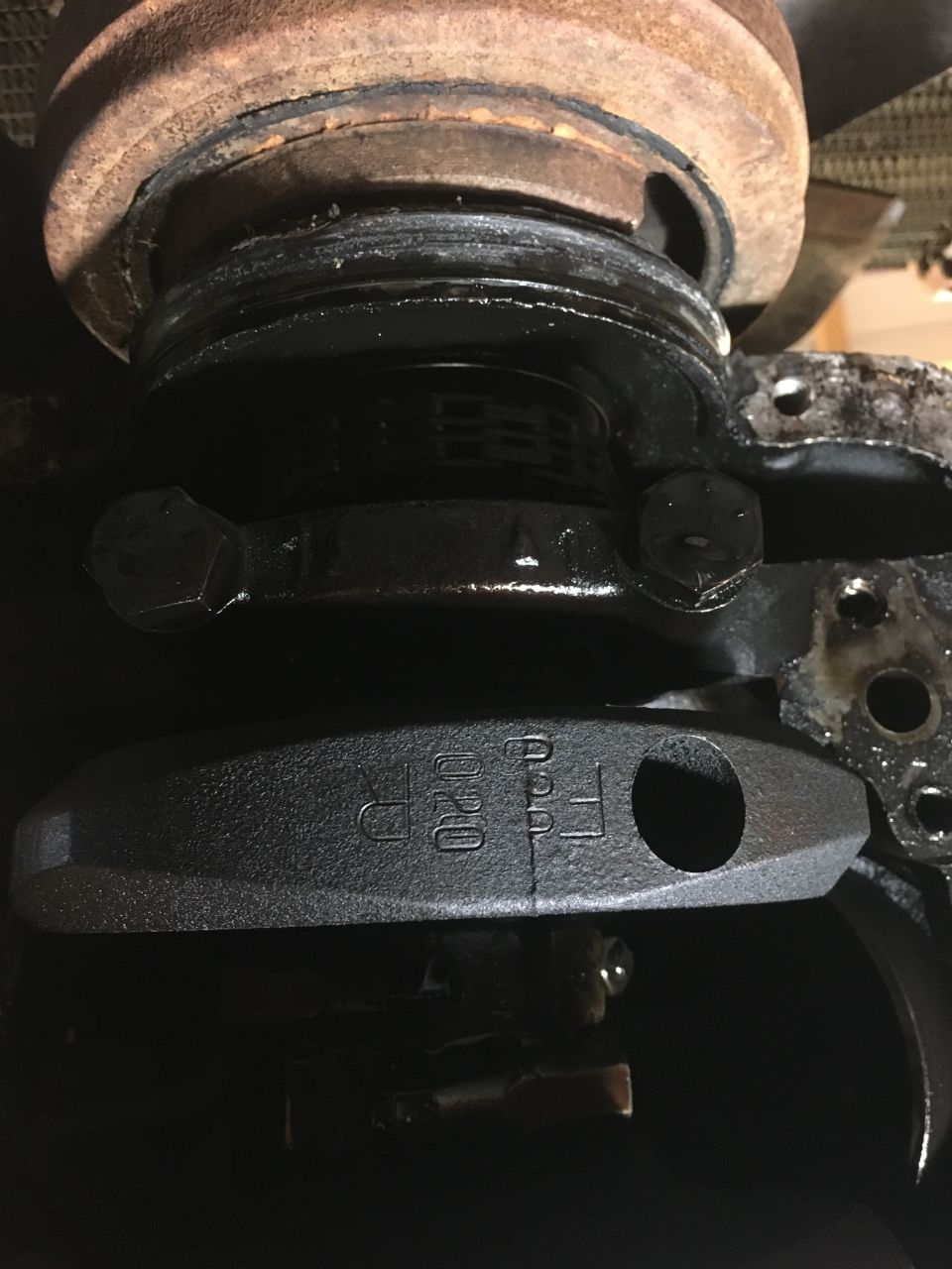 Crankshaft bearing cap with markings 020 and FF, below pulley and rusty flywheel.