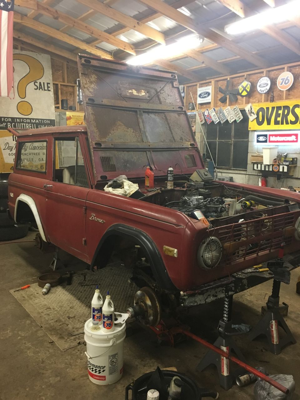 Red 1974 Ford Bronco with hood open, on jack stands in a garage.