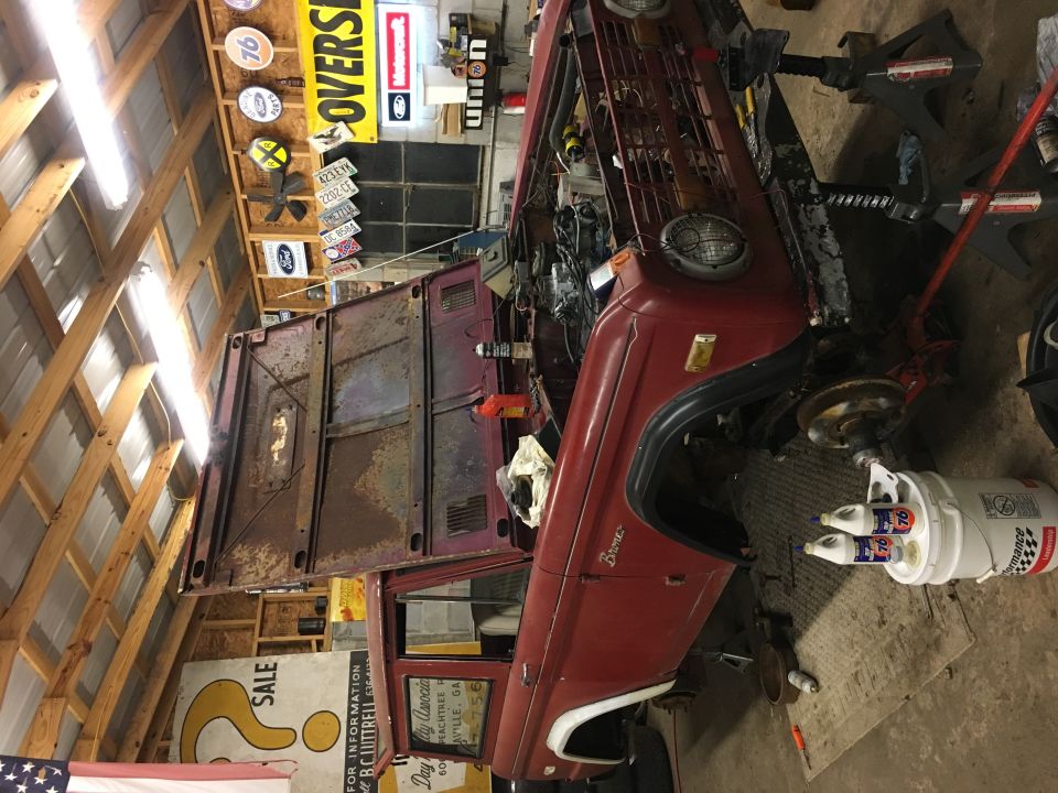 Red 1974 Ford Bronco with hood open, on jack stands in a garage.