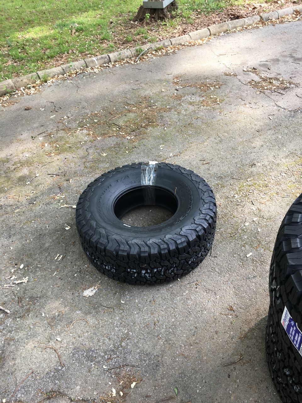 Two BFGoodrich All-Terrain T/A KO2 tires on pavement, one is wrapped in plastic.