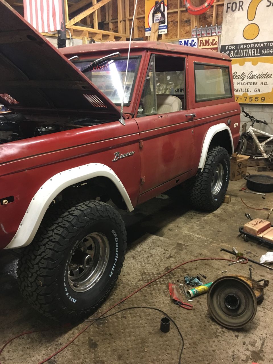 Red 1974 Ford Bronco in a garage with hood open and tools on the floor.