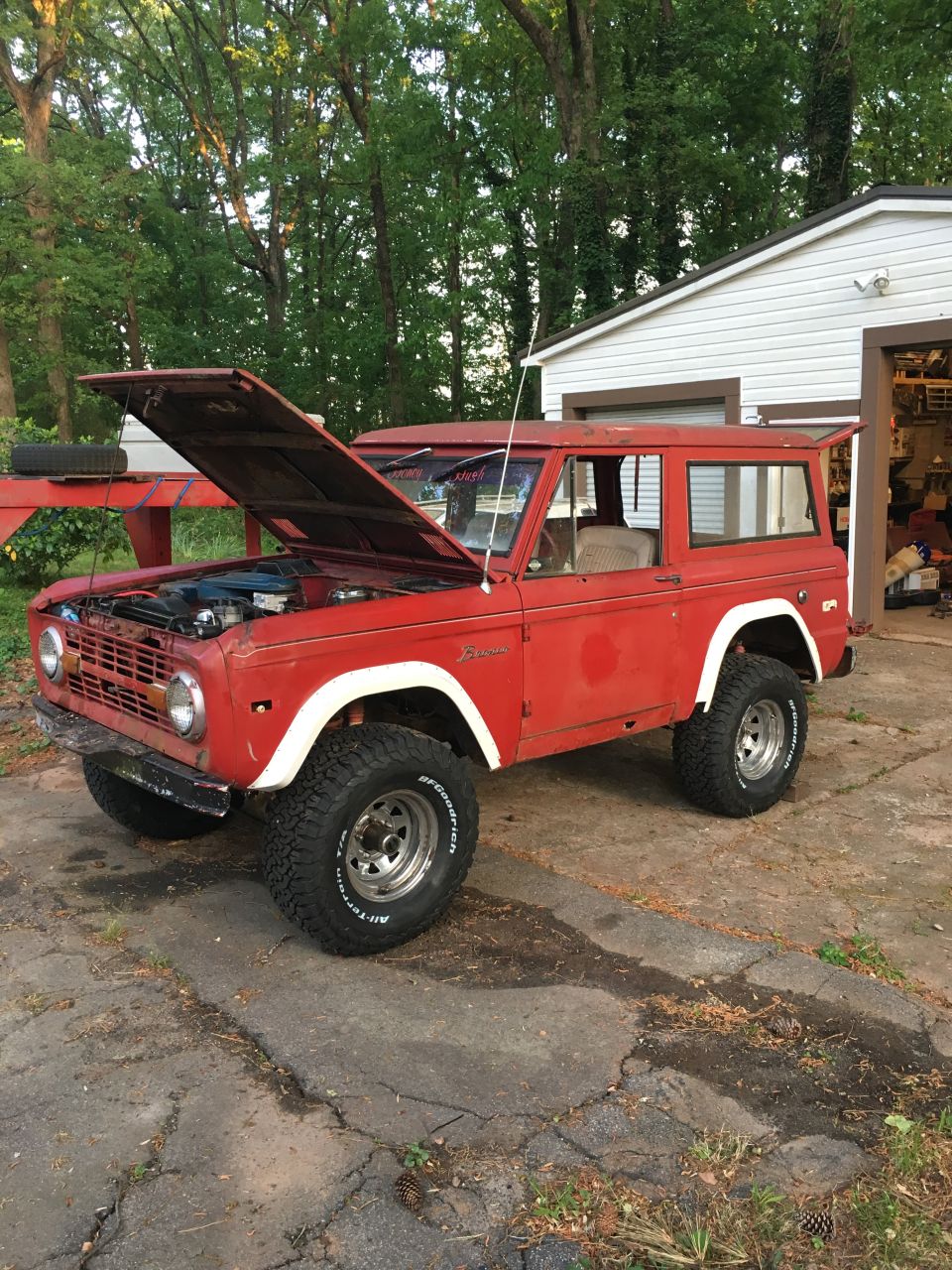 Red 1974 Ford Bronco with hood open, parked on driveway in front of garage.