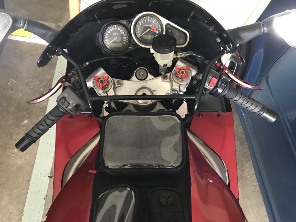 Red motorcycle handlebars, gauges, and front fairing with a tank bag.
