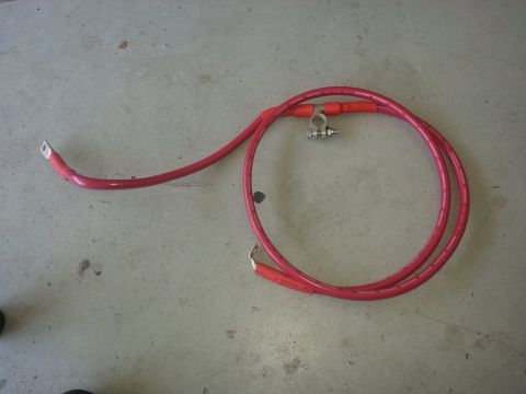 1994 Ford Bronco - Photograph of a fabricated red battery cable with terminal ends on a concrete floor, not a document.