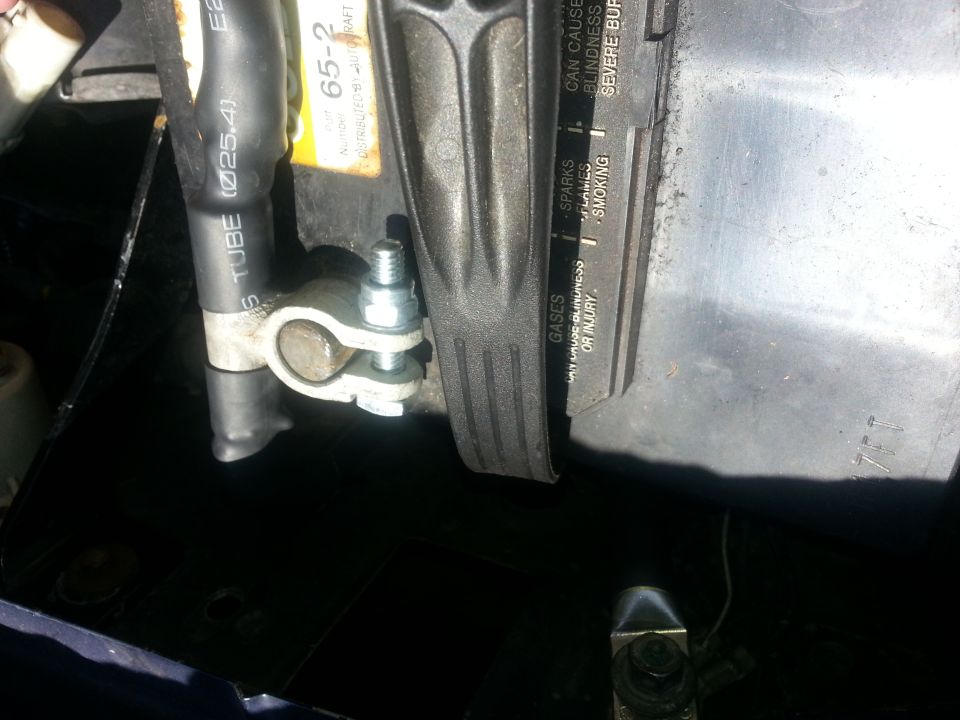 Battery terminal clamp installed on a battery post with warning label