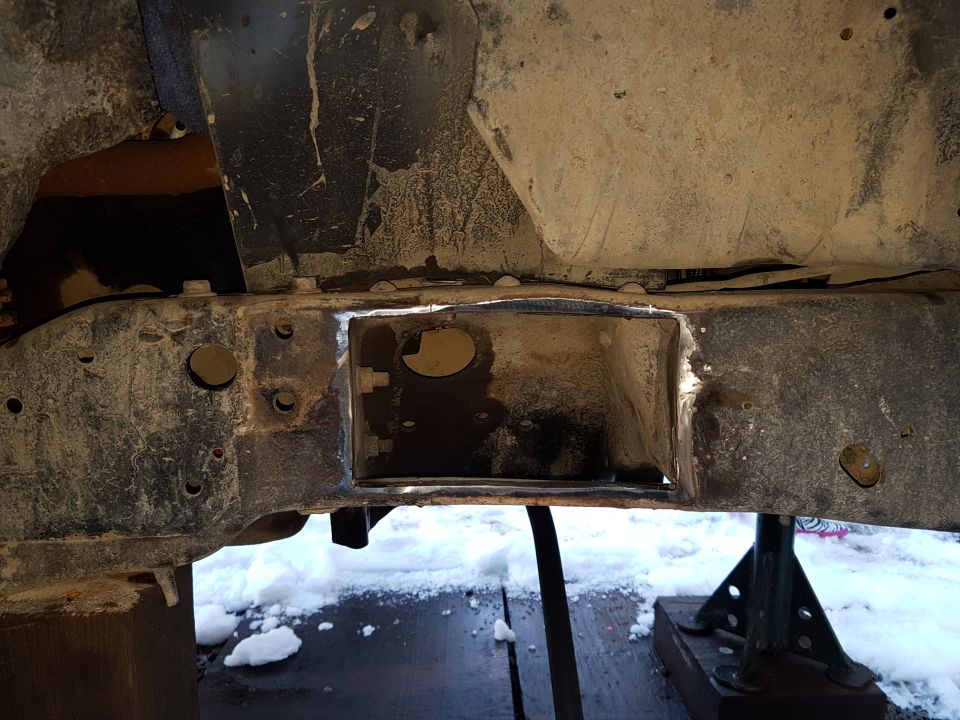 Vehicle frame with a section cut out, supported by jack stands, with snow on the ground.