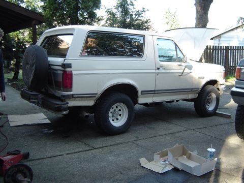 1989 Ford Bronco - White 1989 Ford Bronco with hood up, parked in a driveway with a spare tire mounted on the rear door.