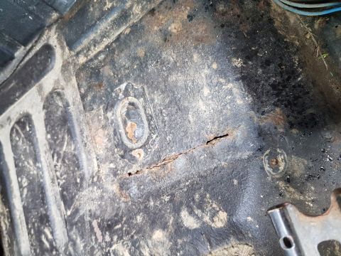 1984 Ford Bronco - This image shows the heavily rusted and corroded floor pan of a vehicle, likely the interior of a 1984 Ford Bronco. The metal is dark with…