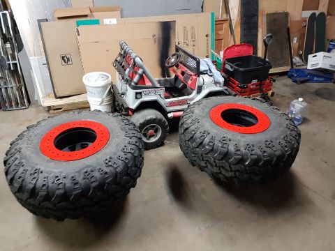 1984 Ford Bronco - Two large off-road tires with red beadlock rings are in the foreground, with a red and white toy Jeep in the background. The scene appears…